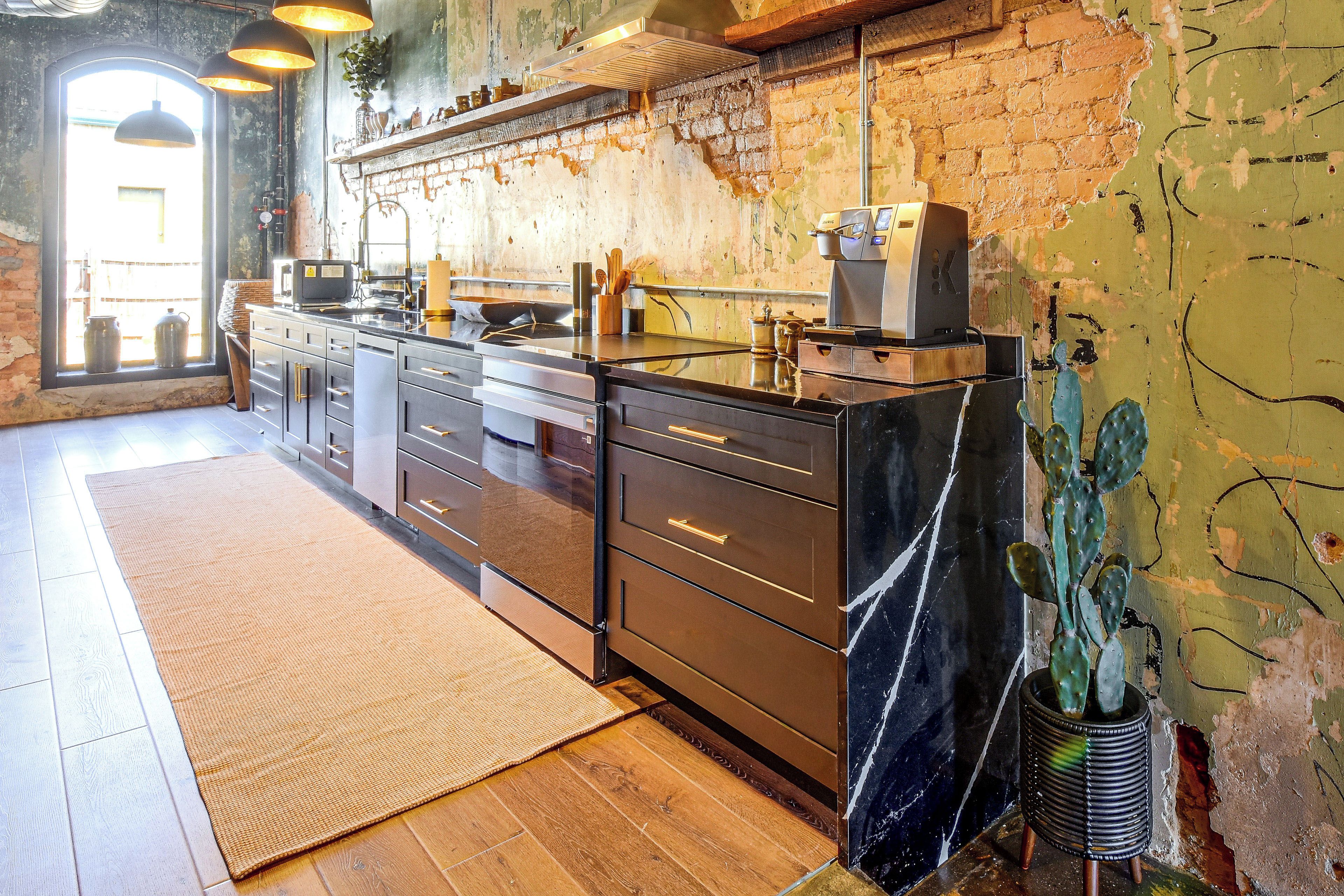 A kitchen with a brick wall, wooden cabinets, and a large window.
