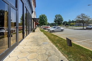 Un parking avec un bâtiment sur la gauche, un trottoir et une zone herbeuse.