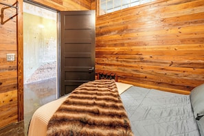 Une pièce aux murs en bois, un lit recouvert d’une couverture à rayures et une porte avec une fenêtre.