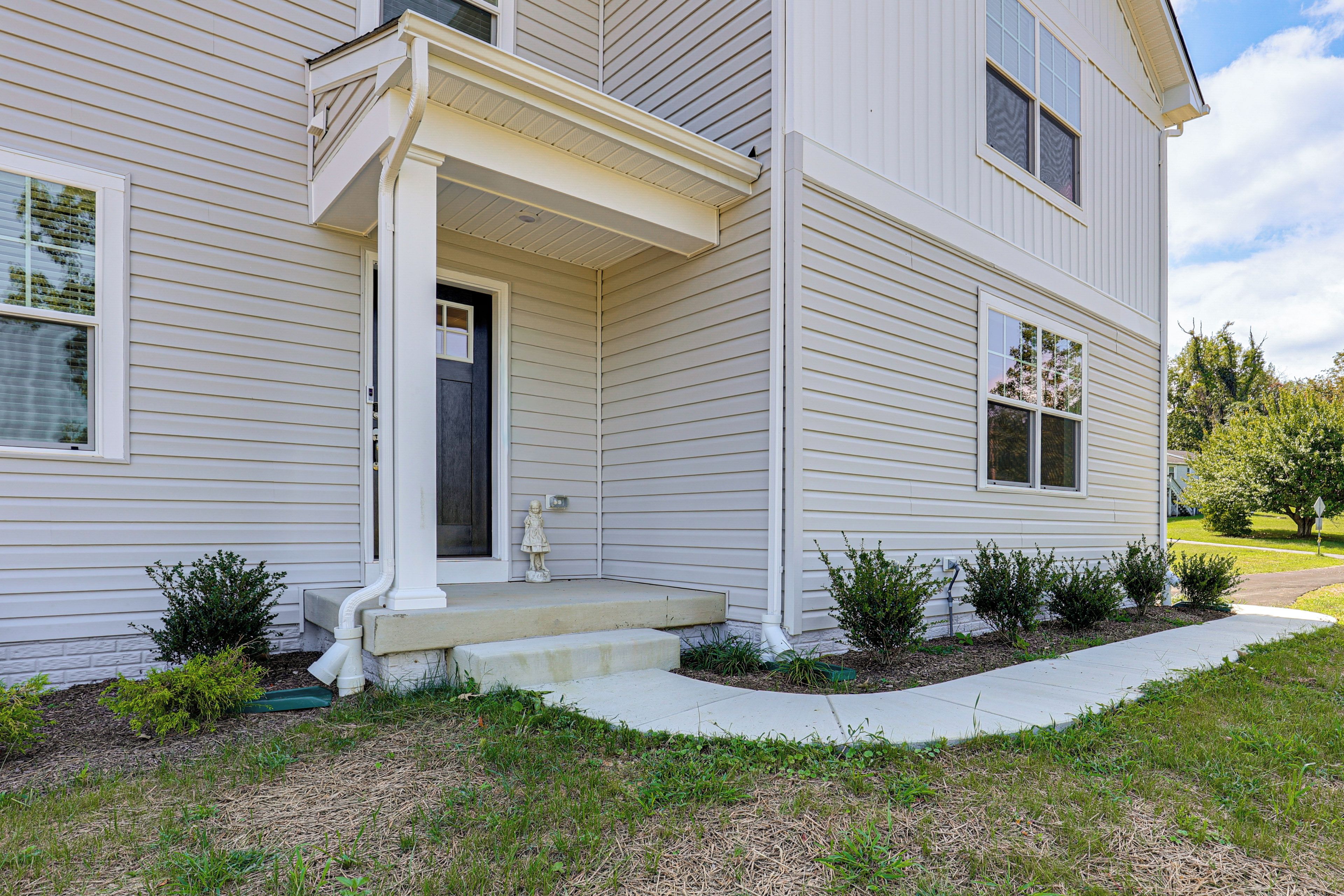 A two-story residential building with a front porch, a mailbox, and a small garden area.