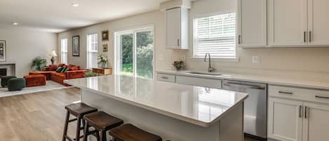 A modern kitchen with a large island, bar stools, and a dining area with a sofa and chairs.