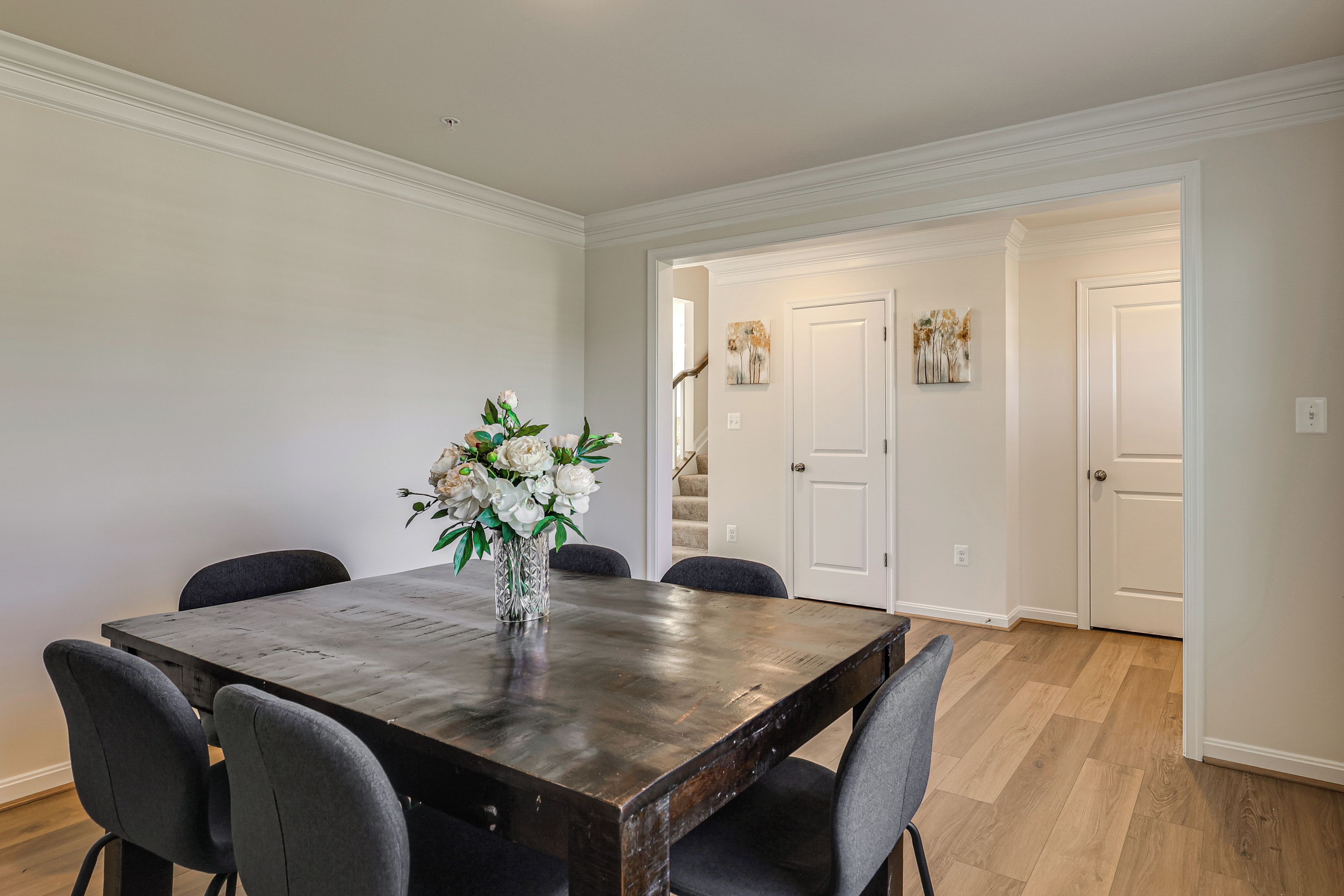 A dining area with a wooden table, six chairs, and a vase of flowers.