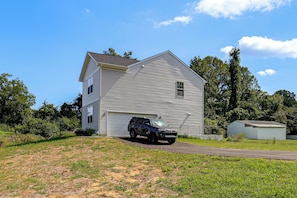 Ein zweistöckiges Haus mit Garage, Auffahrt und einer kleinen Gartenhütte.