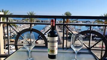 Ein Glastisch mit einer Weinflasche und zwei leeren Weingläsern, mit Blick auf eine Marina und Boote.