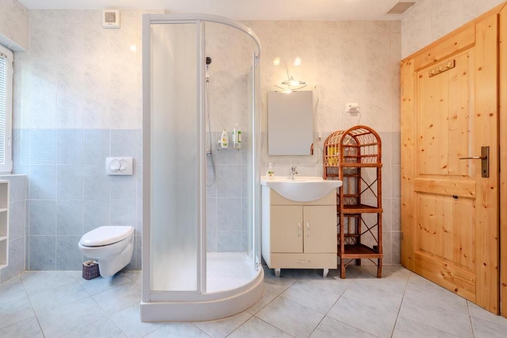 Un baño con ducha envuelta en vidrio, inodoro, lavabo con espejo y un mueble de madera.