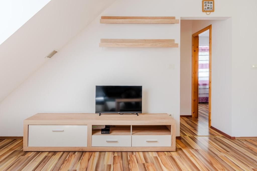 A modern living room with a flat-screen TV on a wooden TV stand, a sloped ceiling, and a wooden floor.
