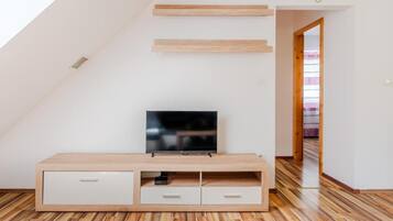 A modern living room with a flat-screen TV on a wooden TV stand, a sloped ceiling, and a wooden floor.