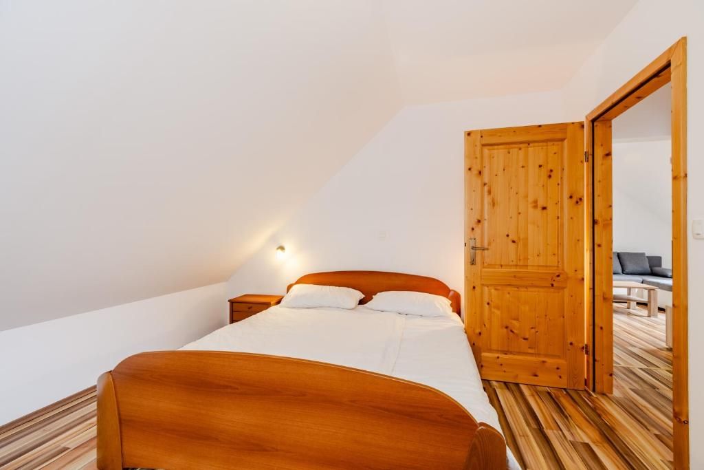 A bedroom with a wooden bed, a nightstand, a wall-mounted light, and an open door leading to another room.