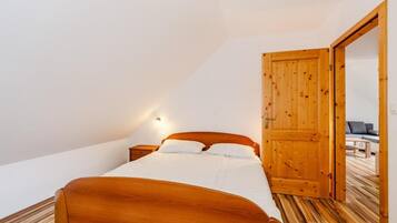 A bedroom with a wooden bed, a nightstand, a wall-mounted light, and an open door leading to another room.