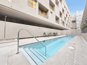 A swimming pool with a metal ladder, surrounded by a concrete deck and a building with balconies. - Welcoming 2-bedroom Loft In Providencia For 5 (Providencia)