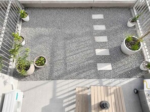 Een terras op het dak met grind, plantenbakken, een houten tafel en een barbecue.