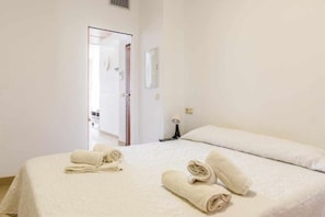 A hotel room with a bed, two rolled towels, a bedside lamp, and a door leading to another room. - Mar Y Sol Caleta Panorama 3A (Algarrobo-Costa)