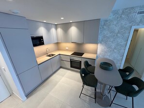 A modern kitchen with a dining area, featuring a built-in oven, a sink, and a dining table with chairs.