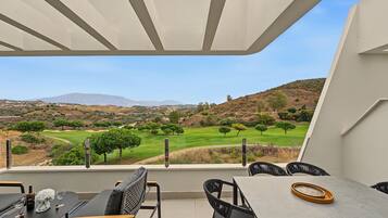 Una terraza con mesa y sillas, vista a un campo de golf y una montaña al fondo.