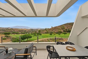 A terrace with a table and chairs, a view of a golf course, and a mountain in the distance.