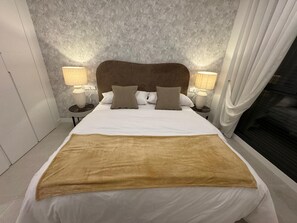 A hotel room with a large bed, two bedside lamps, a headboard, and a view of a fireplace. - Apartment 'Duplex Bahía' with shared pool, private terrace and Wi-Fi (Málaga)
