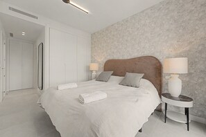 A modern bedroom with a large bed, two bedside tables with lamps, a wardrobe, and a patterned wall.