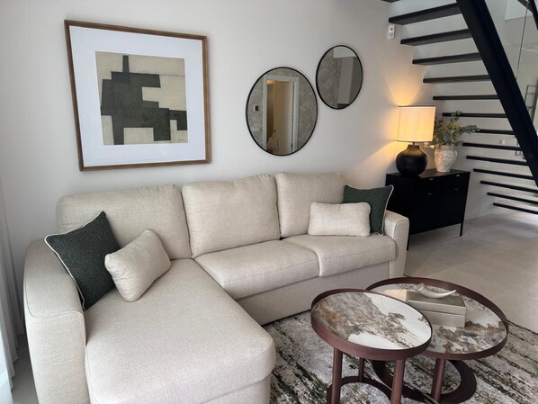 A living room with a beige sectional sofa, two round side tables, and a staircase.