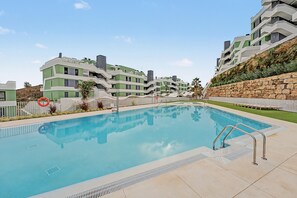 A swimming pool with a clear blue water surface, surrounded by a paved deck.