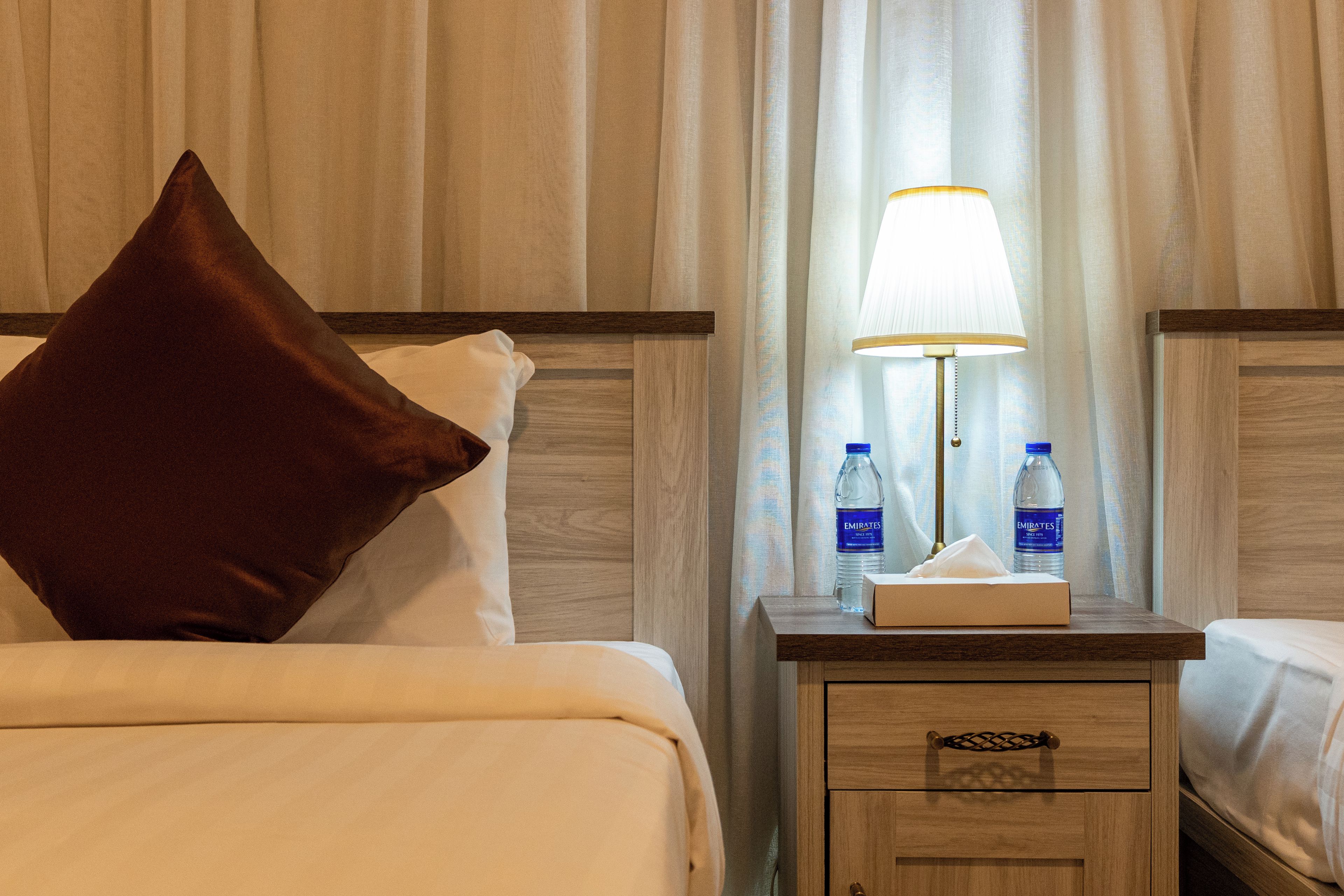 Habitación de hotel con una cama, una mesita de noche, una lámpara y dos botellas de agua.