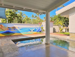 A swimming pool with a colorful mural on the wall, surrounded by a covered area with a view of palm trees and a building. - *VILLA KAP CORAIL* - pool and lagoon (Saint-Paul)