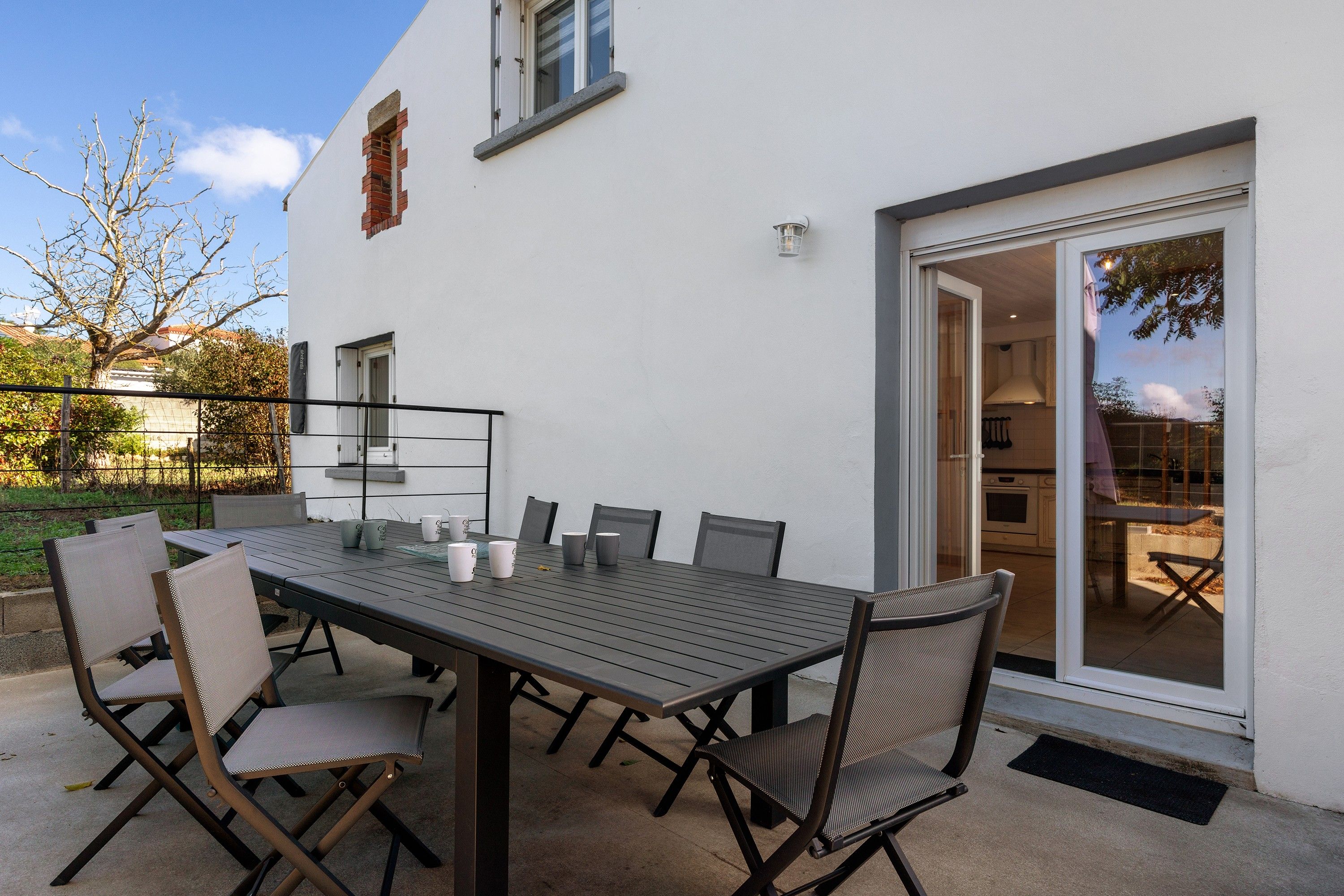Eine Außenpatio mit Tisch und Stühlen, eine Schiebetür zu einer Küche und ein weißes Gebäude mit Fenster und einem kleinen Backsteinbau.