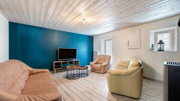Una sala de estar con una pared azul, piso de madera, un televisor de pantalla plana, dos sofás de cuero y un ventanal con persianas.