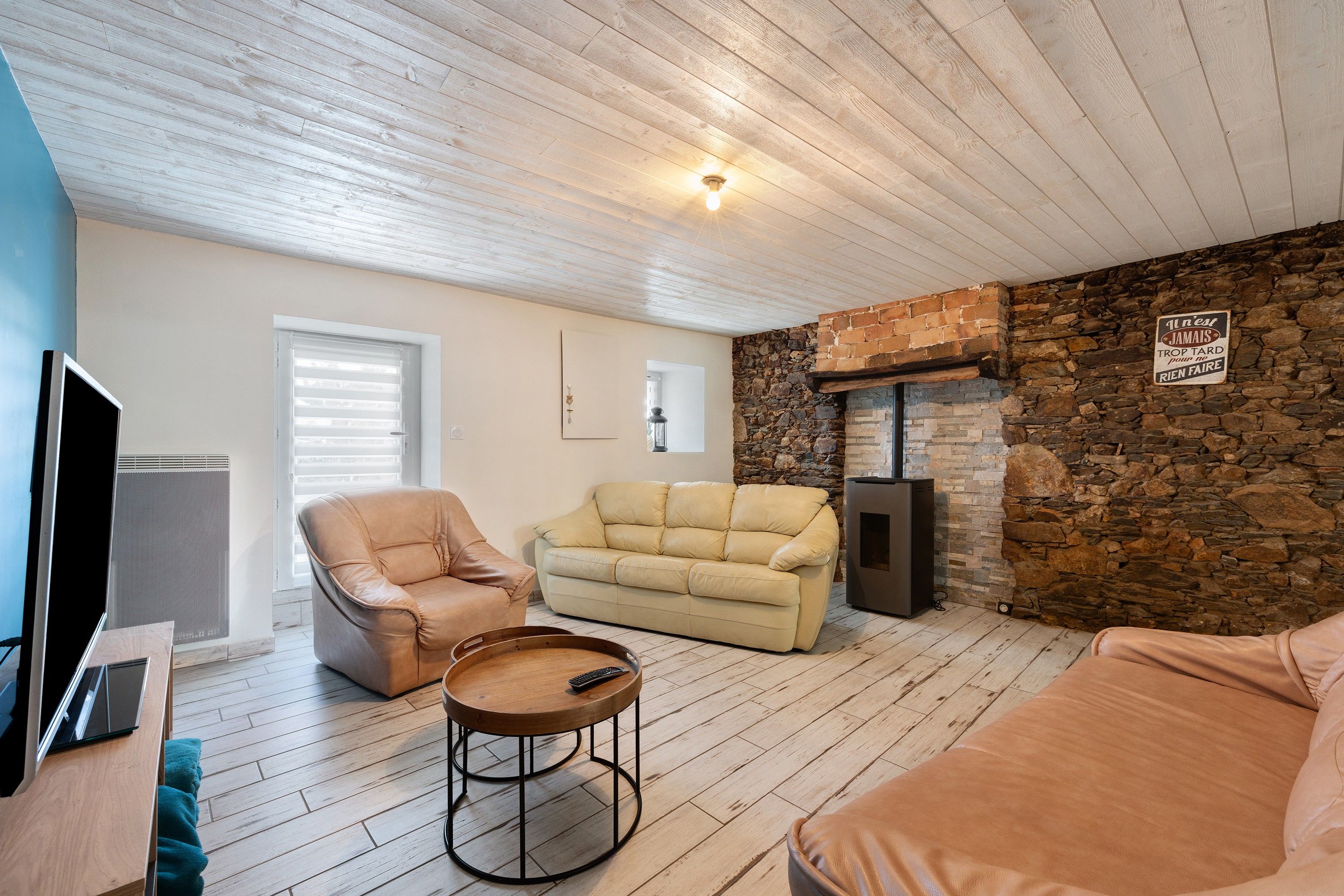 Una sala de estar acogedora con una pared de piedra, una chimenea, un sofá, un sillón y un televisor.