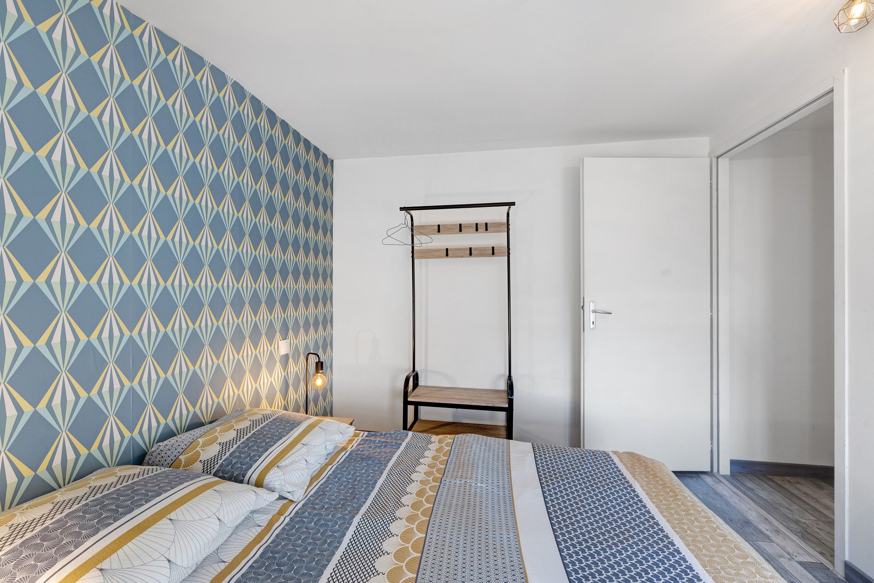Un dormitorio con pared estampada, cama con muchos cojines, una lámpara colgante y una puerta.