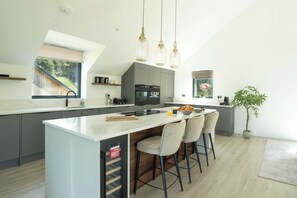 A modern kitchen with a central island, bar stools, and pendant lighting. - Luttrell House - 3 bed eco house (Somerset)