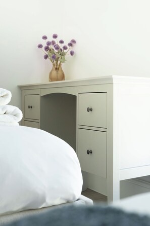 A bedroom with a bed, a dresser with drawers, and a vase with flowers on top. - Luttrell House - 3 bed eco house (Somerset)