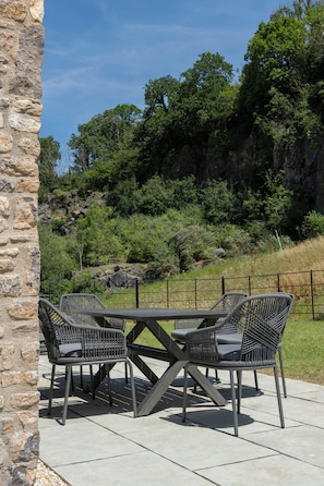 Un área de estar al aire libre con un muro de piedra, una mesa y cuatro sillas.