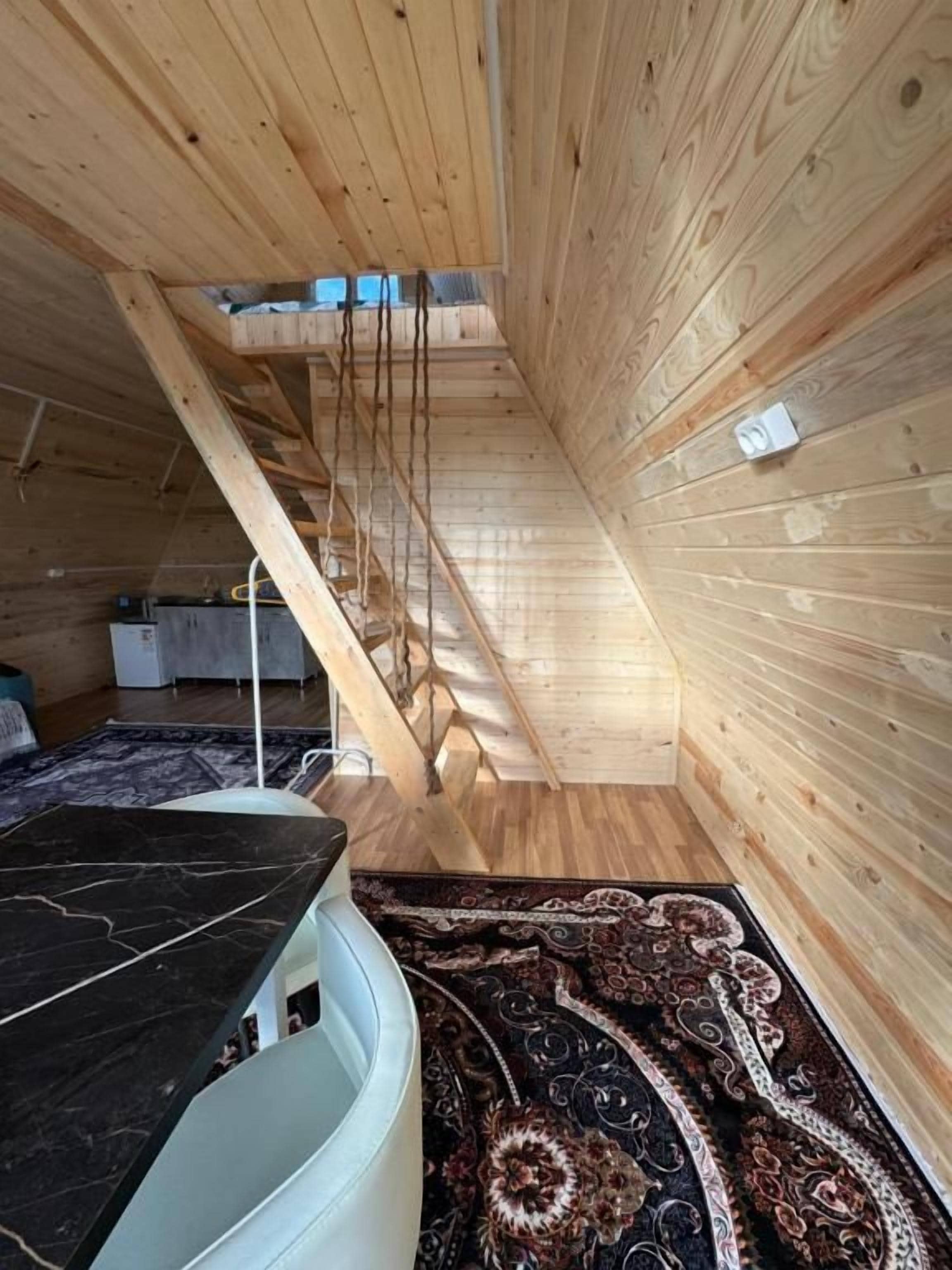 Une pièce avec un plafond en pente, des murs en bois, une table en marbre noir et un tapis à motifs.