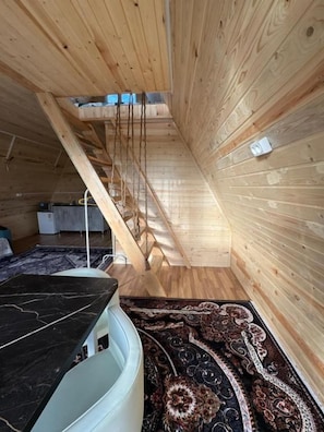 Una habitación con techo inclinado, paredes de madera, una mesa de mármol negro y una alfombra estampada.