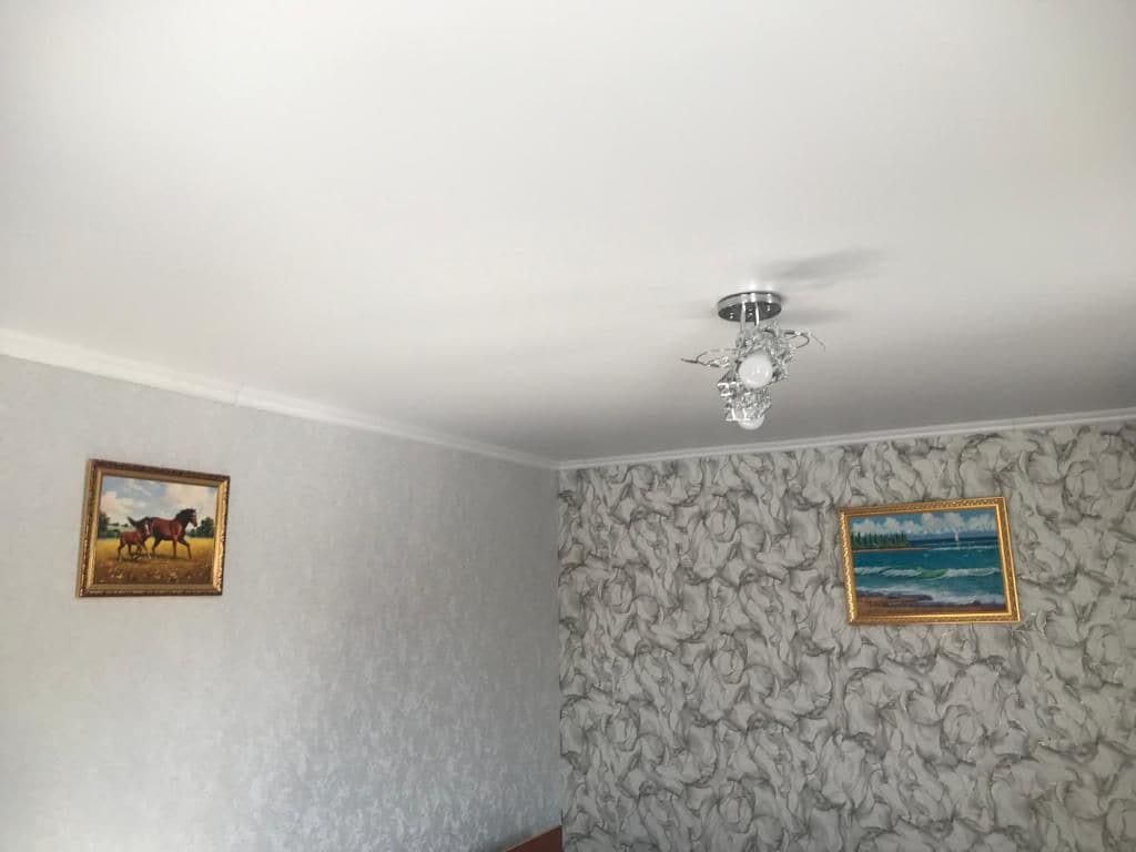 A room with a textured wallpaper, a ceiling fan, and two framed pictures on the walls.