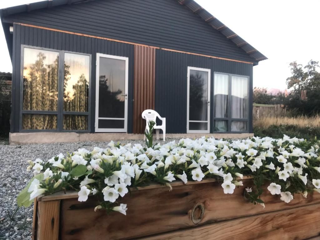 Et moderne hus med store vinduer, en træplantekasse med hvide blomster og en hvid plastikstol.