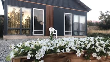 Et moderne hus med store vinduer, en træplantekasse med hvide blomster og en hvid plastikstol.