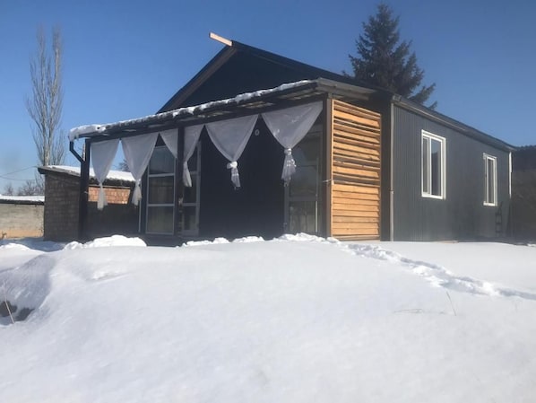 Un edificio de una planta con un porche cubierto y el suelo cubierto de nieve.