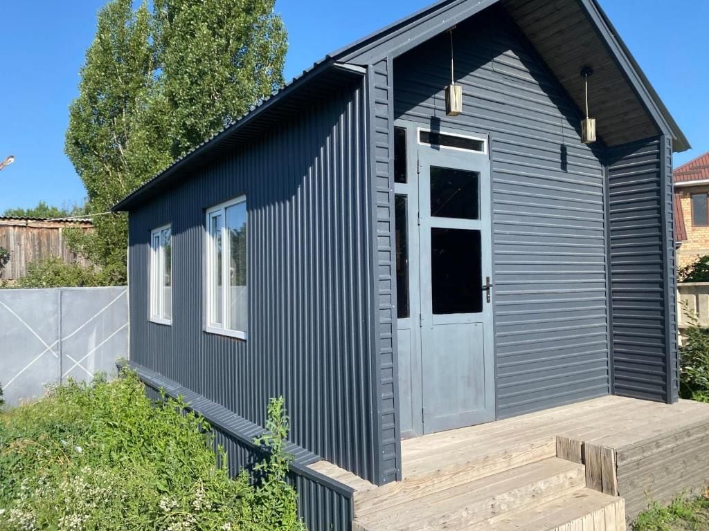 Een modern gebouw met twee verdiepingen, een grijze gevel, een houten terras en een heldere lucht.