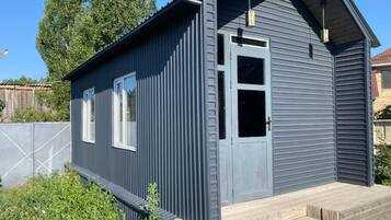 Een modern gebouw met twee verdiepingen, een grijze gevel, een houten terras en een heldere lucht.