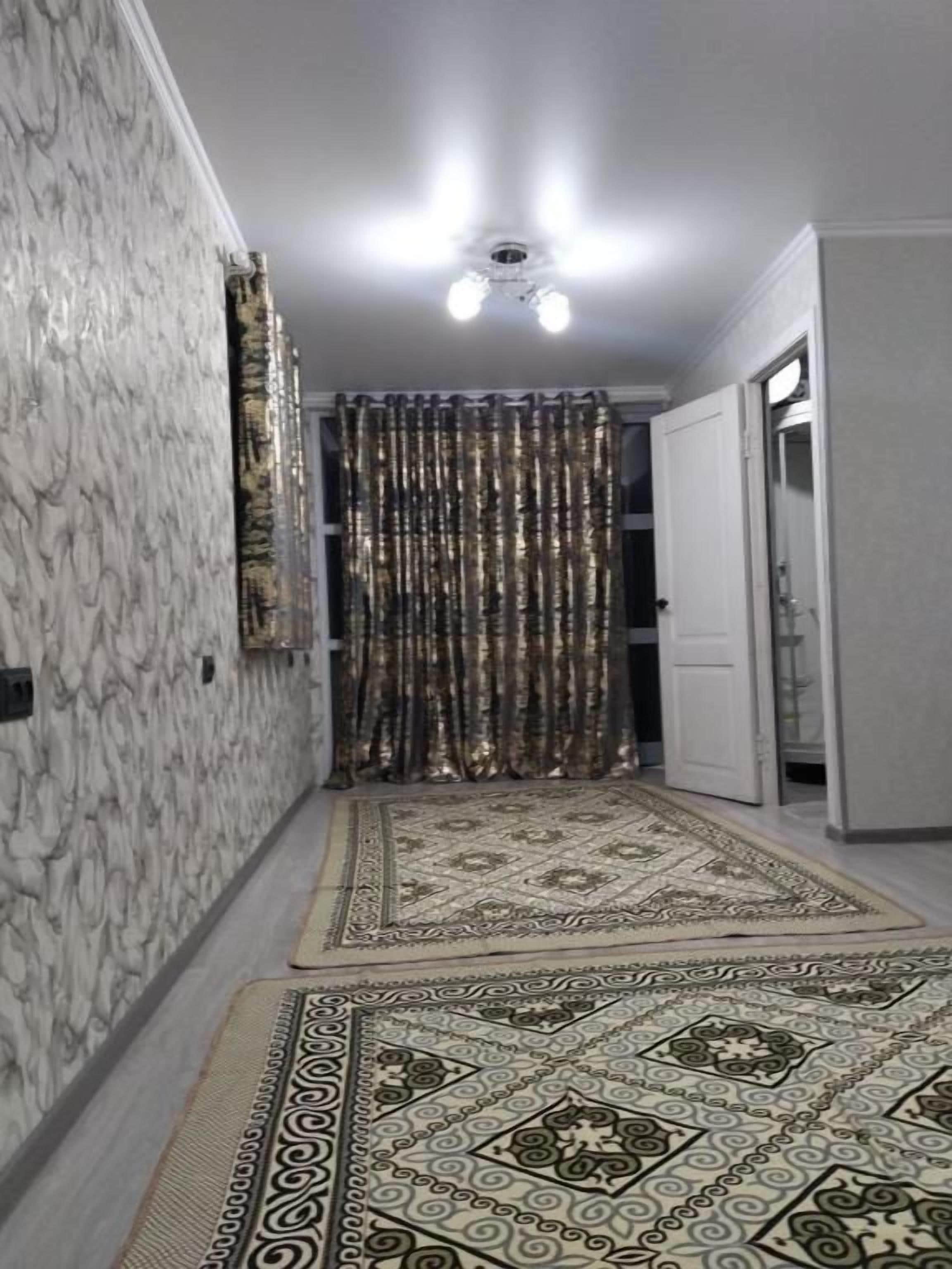 A hallway with patterned rugs, a ceiling light fixture, and a door leading to another room.