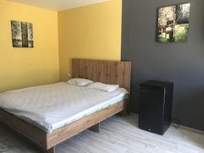 Un dormitorio con una cama de madera, un pequeño armario negro y dos obras de arte en la pared.
