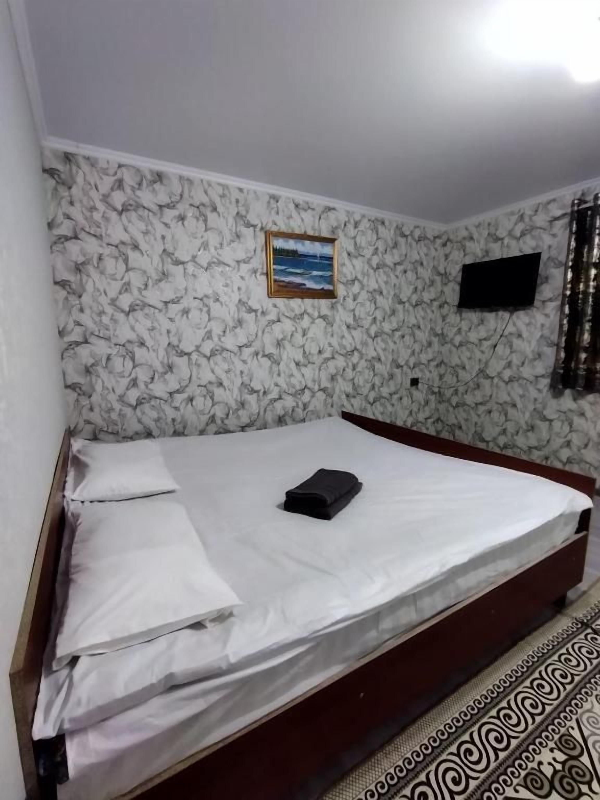 A room with a bed, a television mounted on the wall, and a patterned wallpaper.