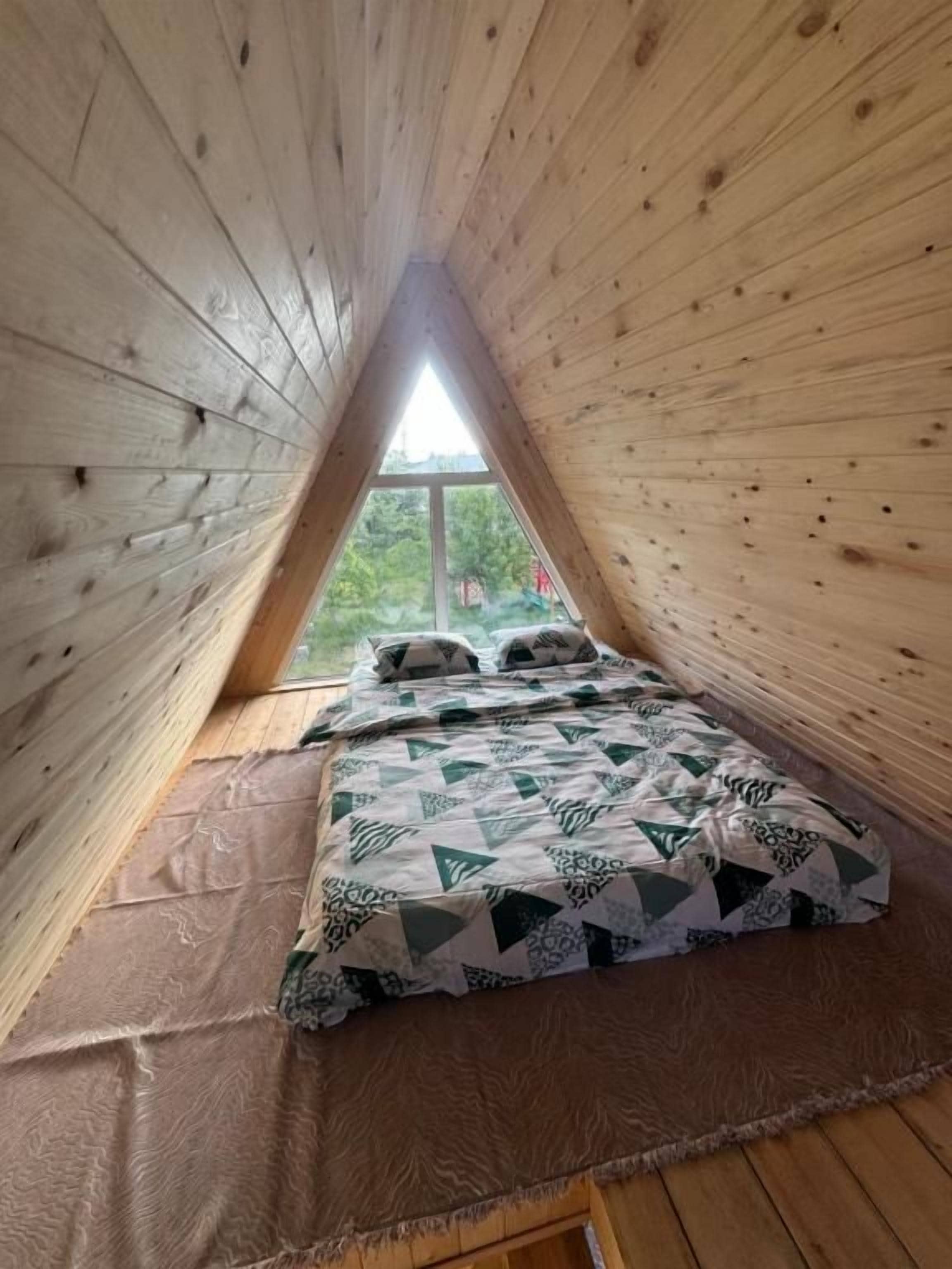 Une pièce triangulaire en bois, avec un lit et une fenêtre.