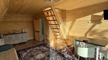 A wooden interior with a loft bed, a dining table, and a staircase.