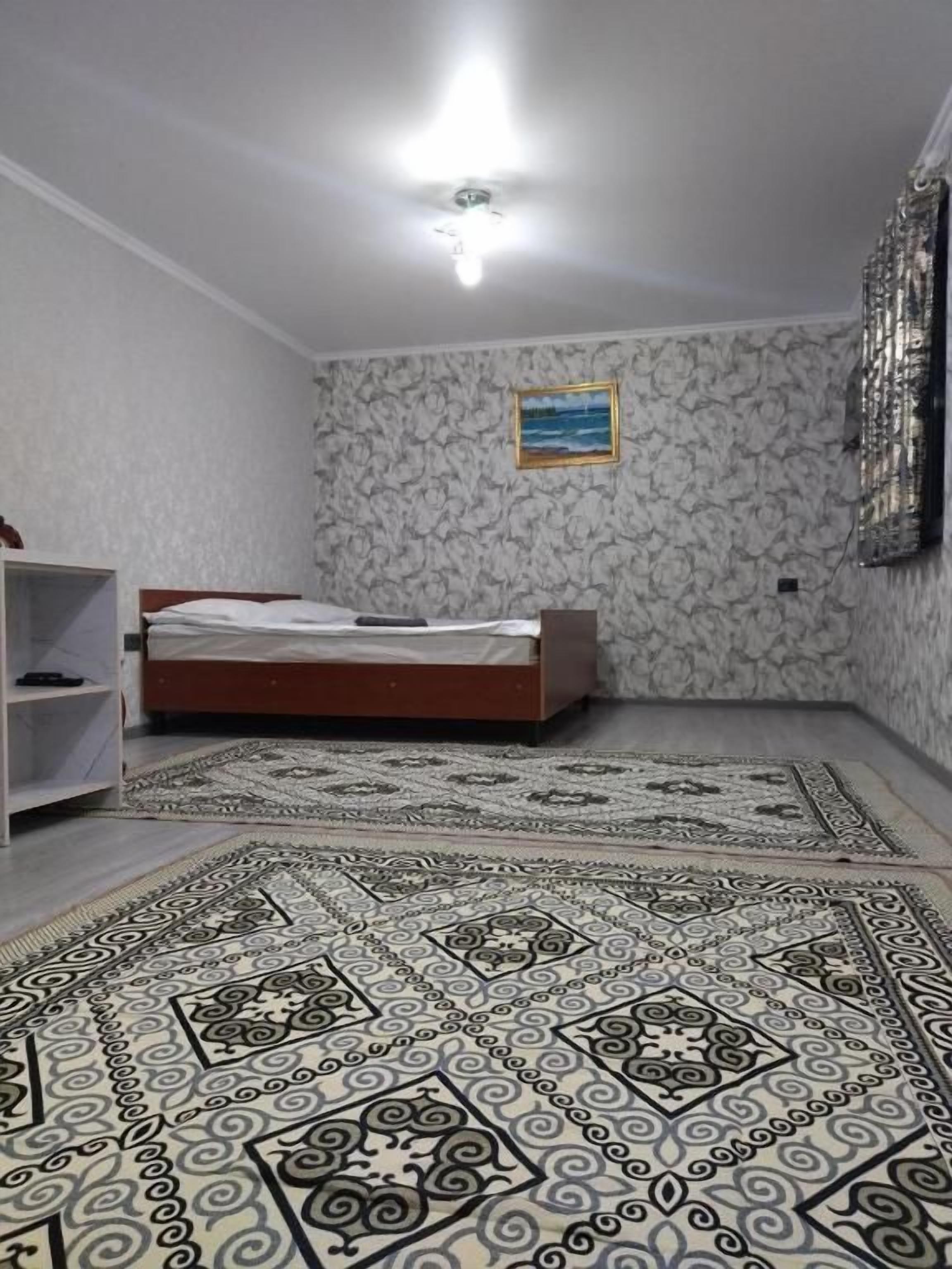 A bedroom with a bed, a patterned rug, a shelf, and a painting on the wall.