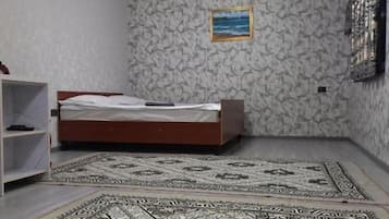 A bedroom with a bed, a patterned rug, a shelf, and a painting on the wall.