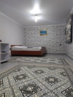 A bedroom with a bed, a patterned rug, a shelf, and a painting on the wall.