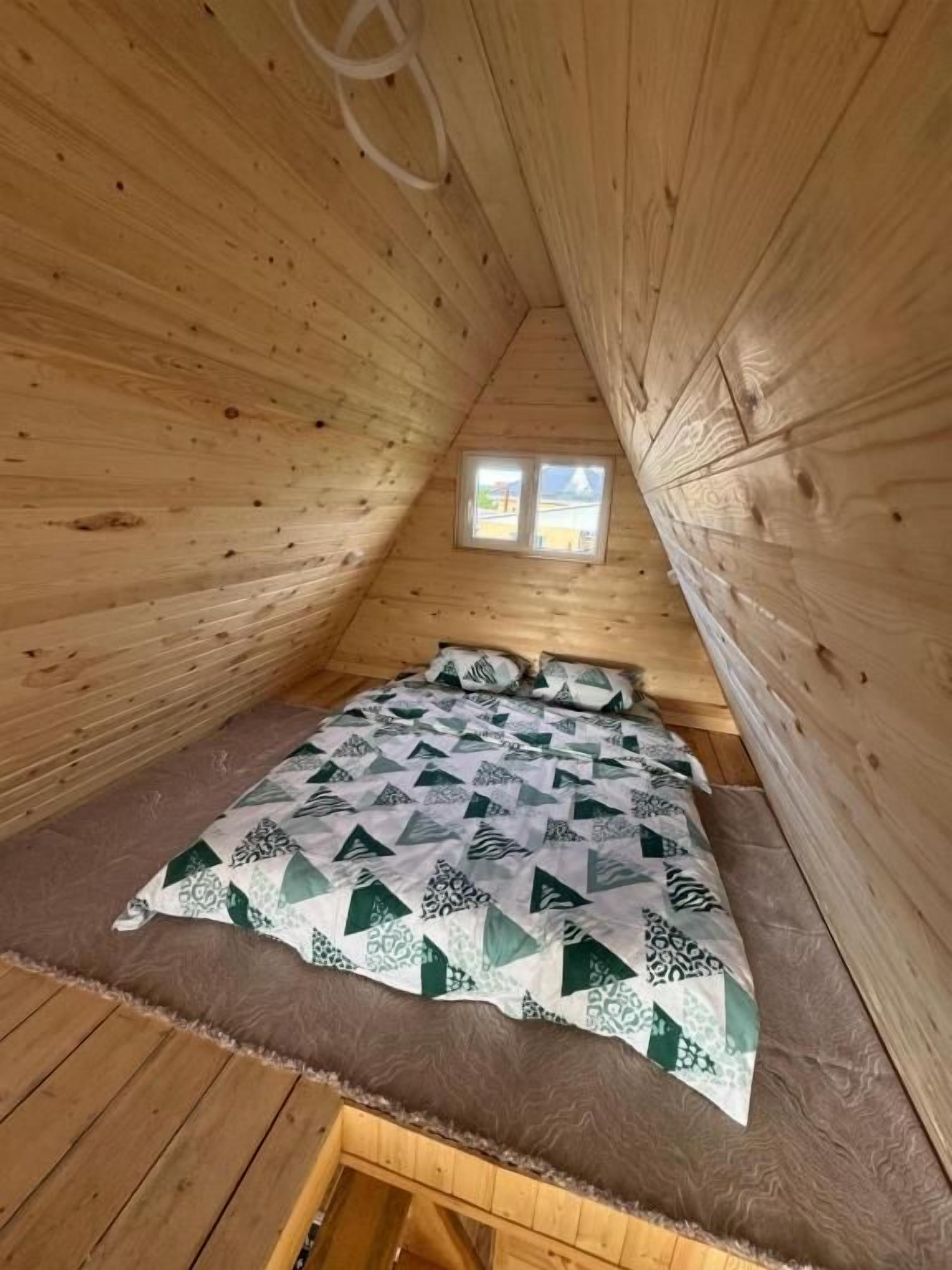 Une petite pièce en bois, avec un lit, une fenêtre et un plafond en pente.