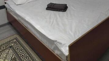A single bed with a wooden frame and white bedding, a patterned wallpaper on the wall, and a patterned rug on the floor.